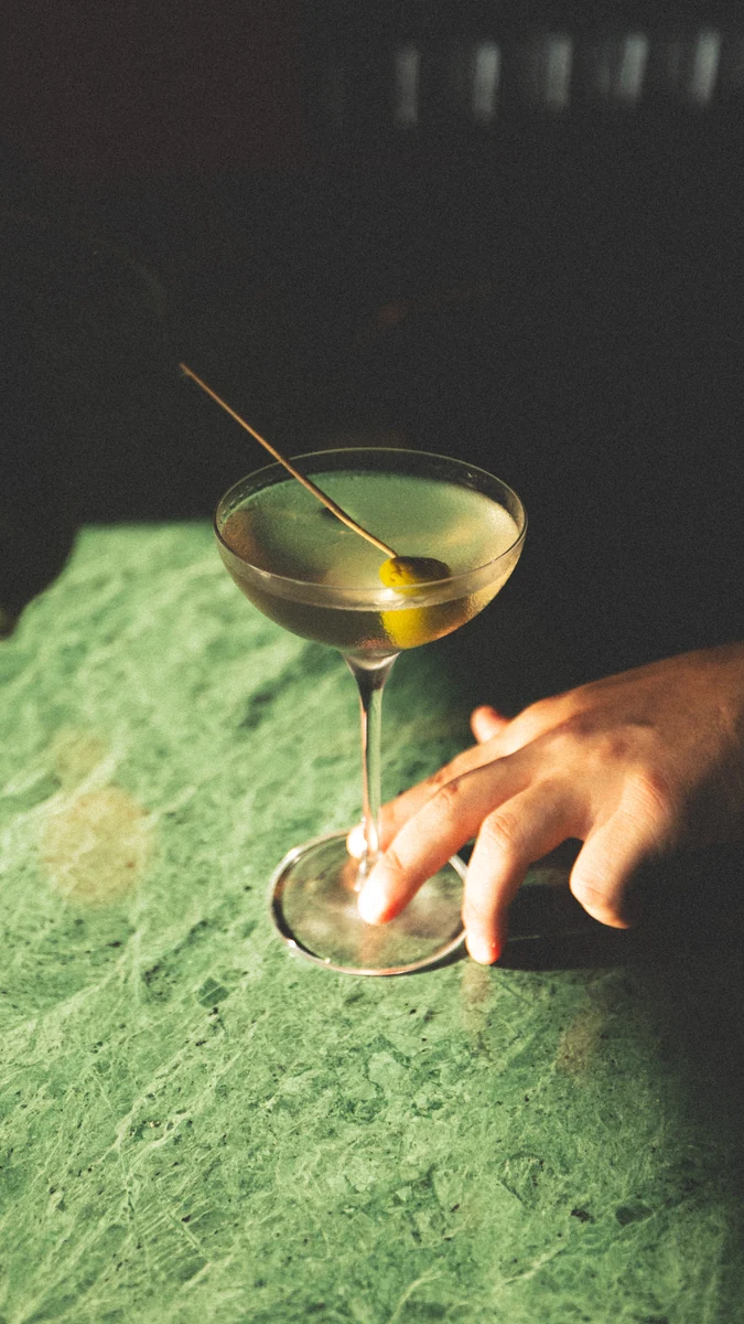 A hand beside a cocktail glass on green marble